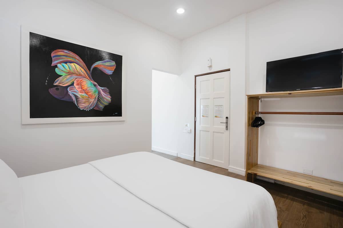 Ein Hotelzimmer mit einem Bett, einem Fischgemälde, einer Tür und einem Fernseher auf einem Regal.
