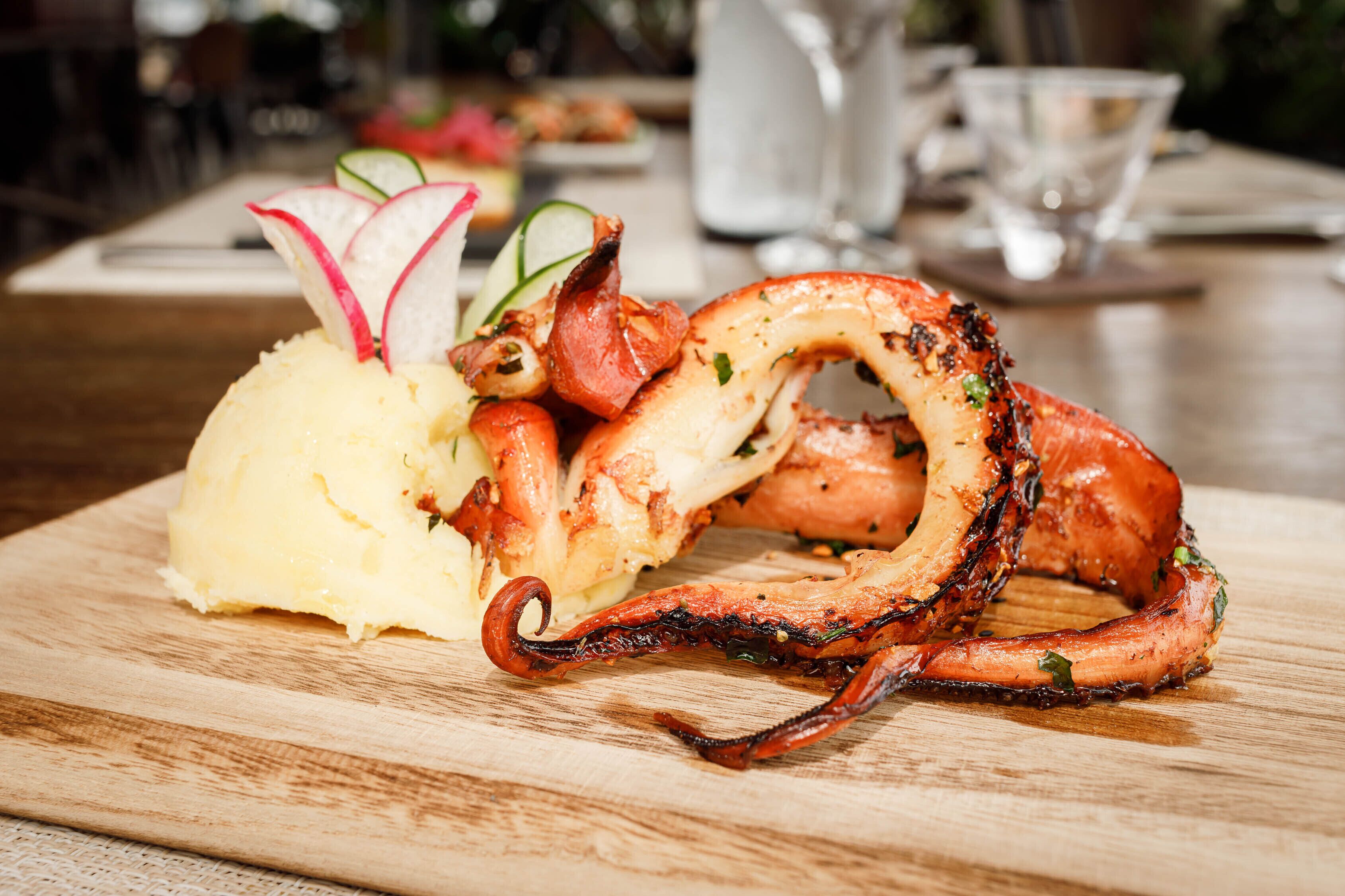 A seafood dish with grilled octopus and a side of mashed potatoes on a wooden board.
