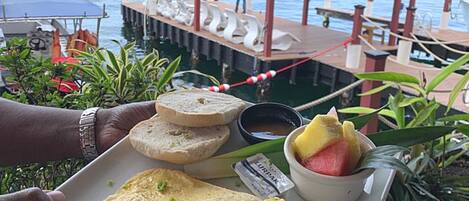 Una persona sosteniendo un plato con comida, un barco al fondo y un muelle.