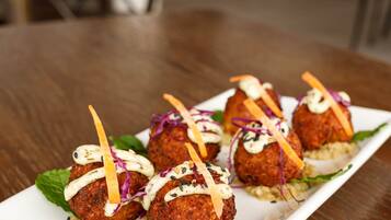 A plate of falafel balls on a white rectangular plate, garnished with vegetables and a white sauce, placed on a wooden table in a restaurant setting.