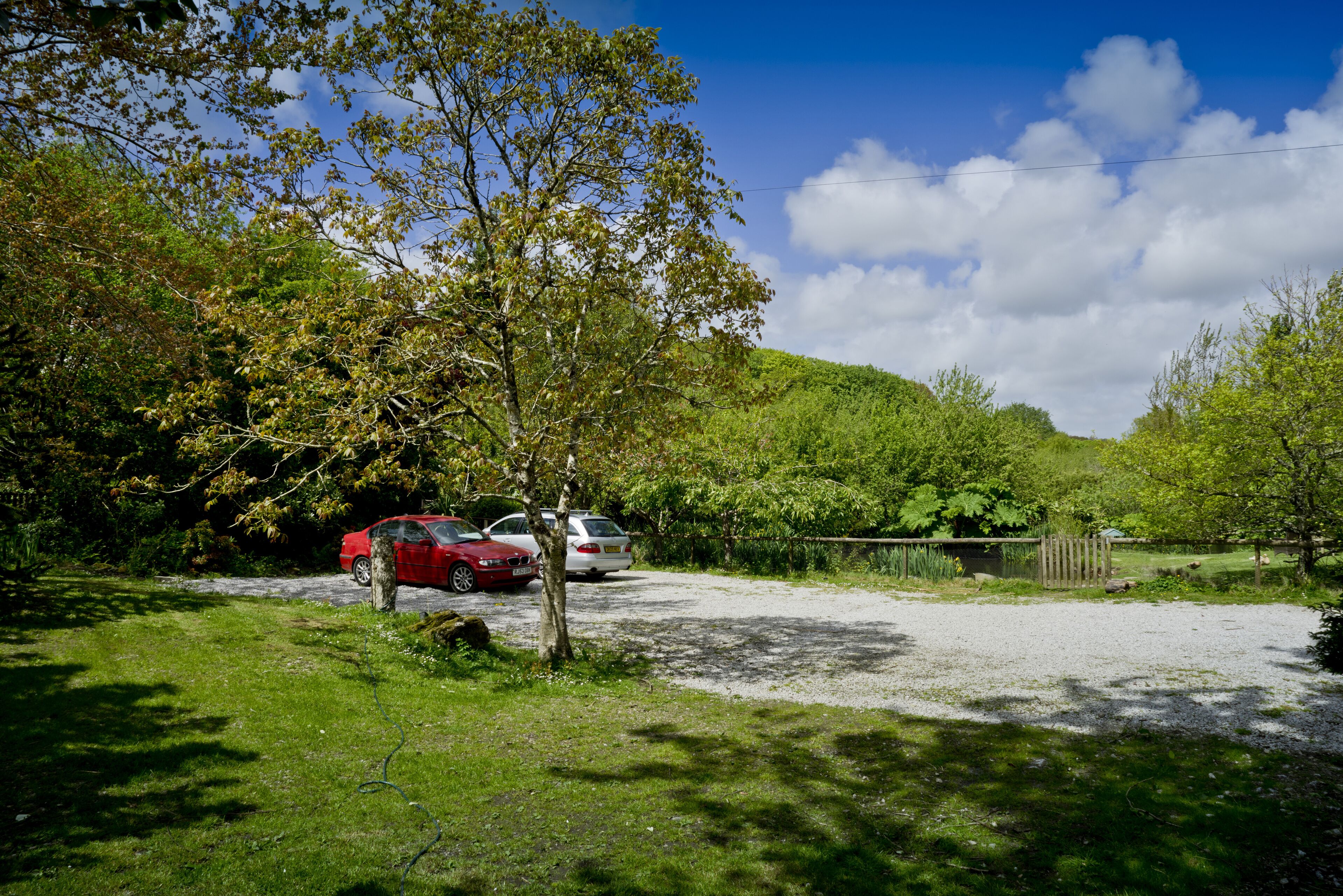 A parking area with two cars, surrounded by trees and a hill in the background.