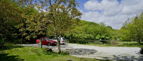 A parking area with two cars, surrounded by trees and a hill in the background.