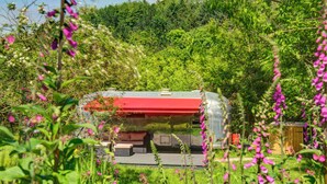 Una cabaña rústica con techo rojo, rodeada de vegetación exuberante y flores silvestres.