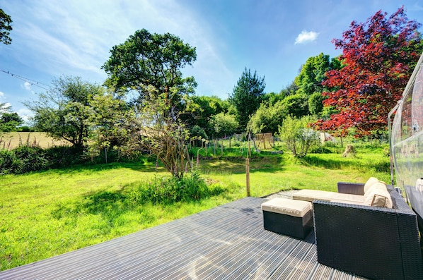 A deck with outdoor seating, surrounded by a lush garden with various trees and shrubs.