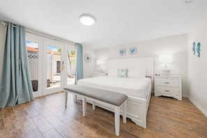 A bedroom with a large bed, a bench, a nightstand, and a view of the outside. - Bianco Sands by Beachside Management (Siesta Key)