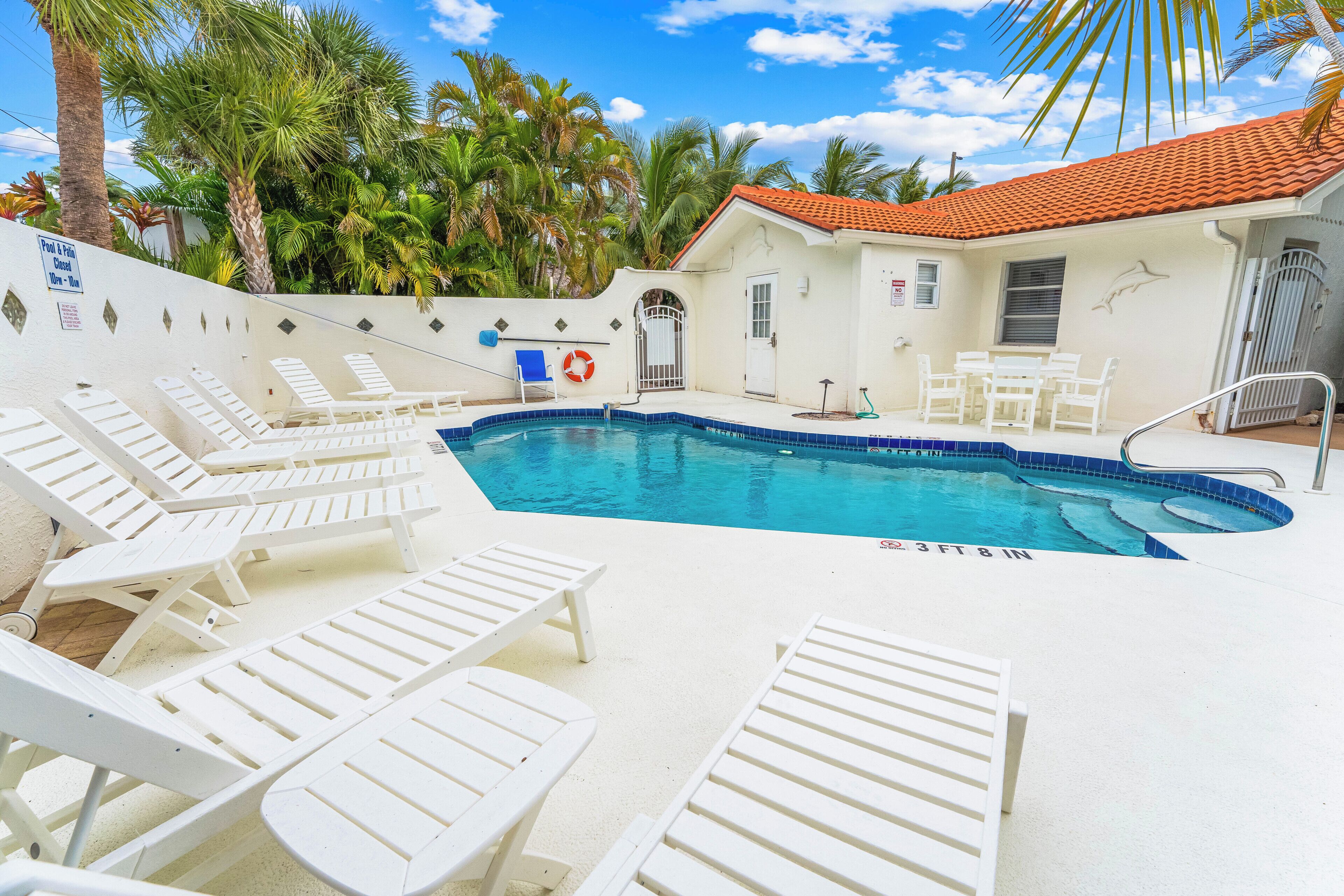 A pool area with white lounge chairs, a lifebuoy, and a palm tree.