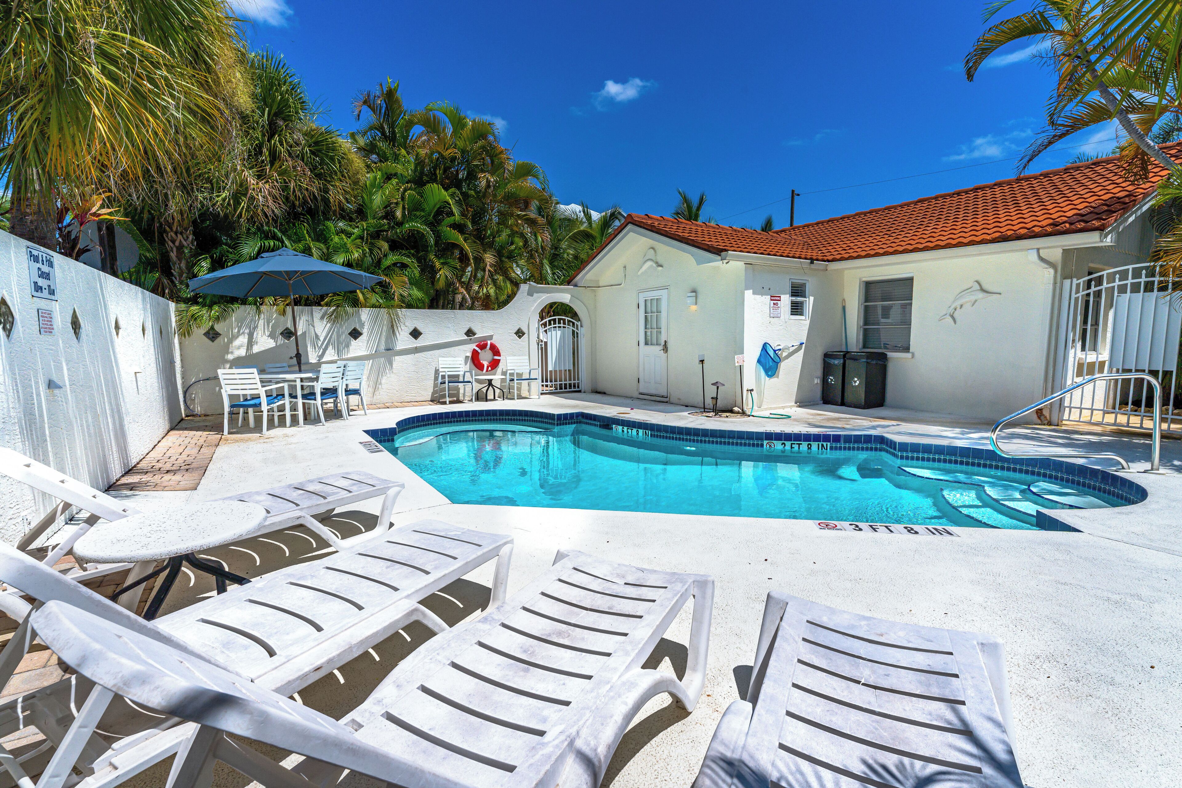 A swimming pool with lounge chairs, a covered seating area, and a building with a tiled roof.