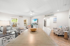 A modern living room with a dining table, a sofa, and a TV. There is a sign that says "MERMAIDS" on the wall. - Bianco Sands by Beachside Management (Siesta Key)