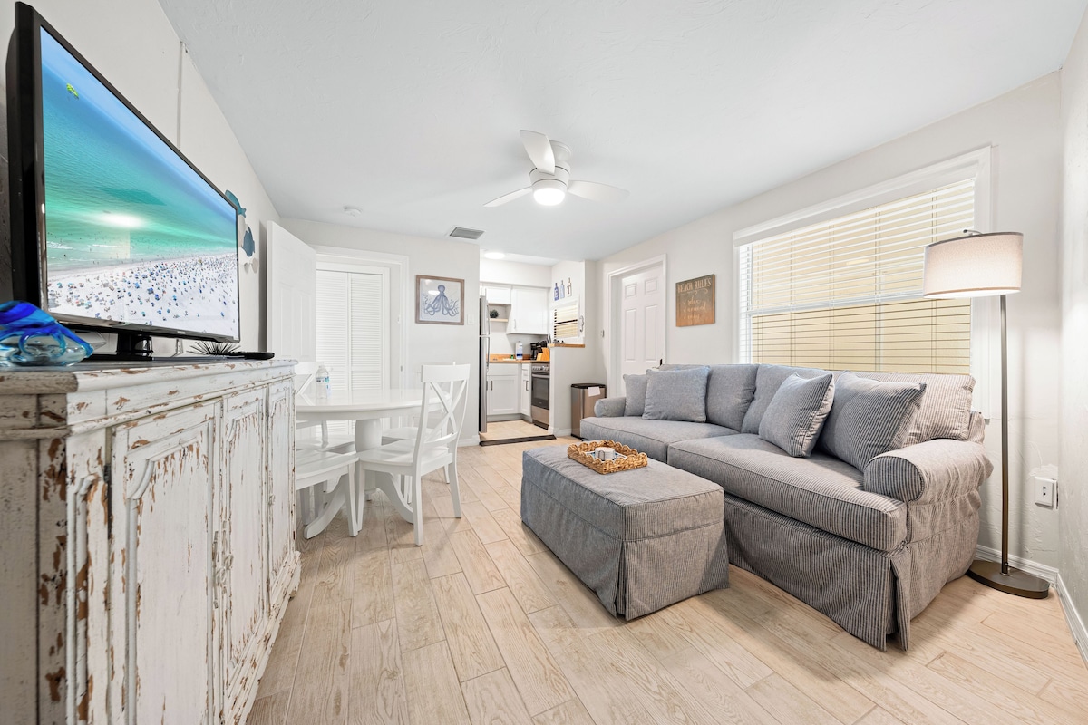 A living room with a television, white furniture, a grey sofa, and a ceiling fan.