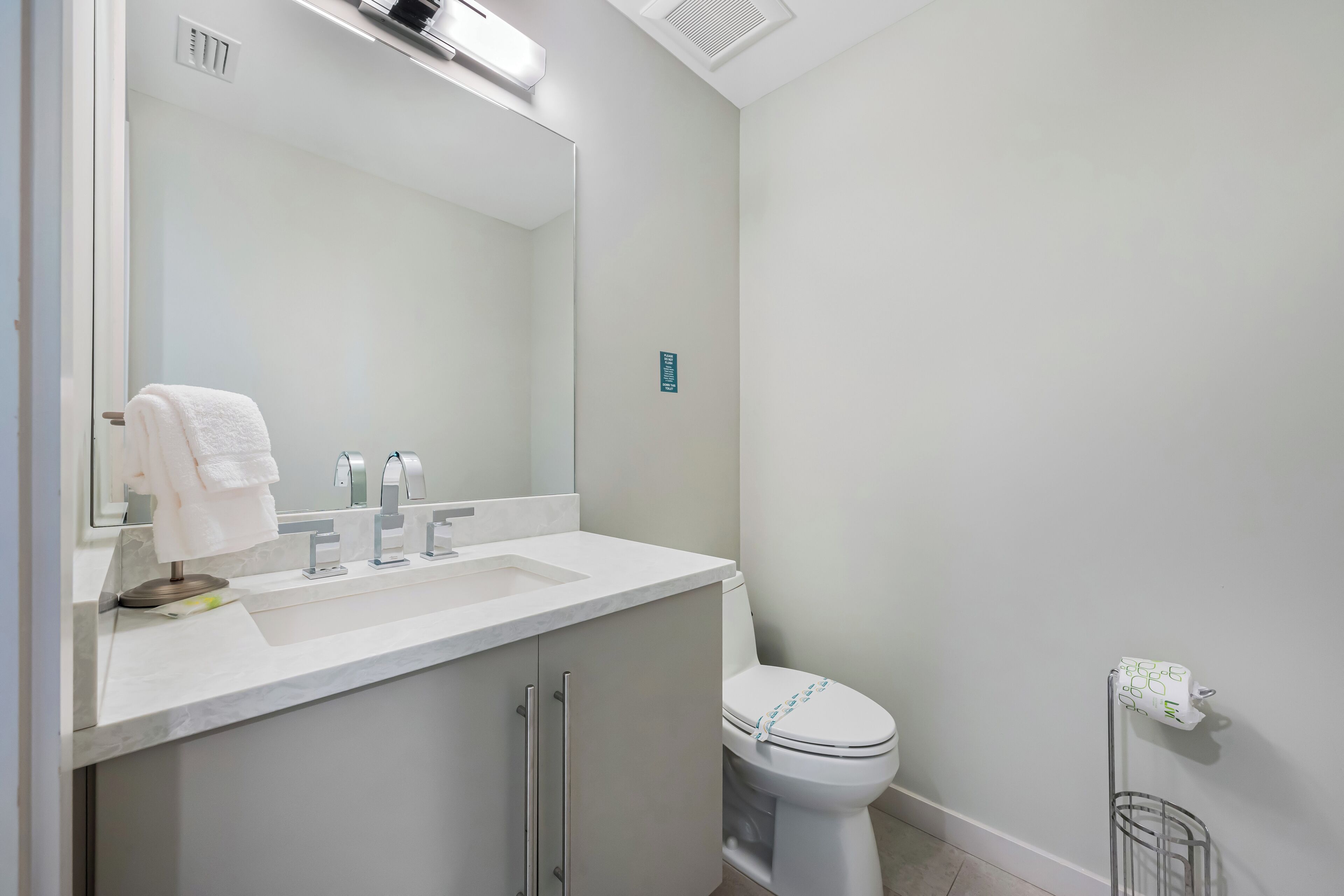A modern bathroom with a white sink, mirror, and toilet.