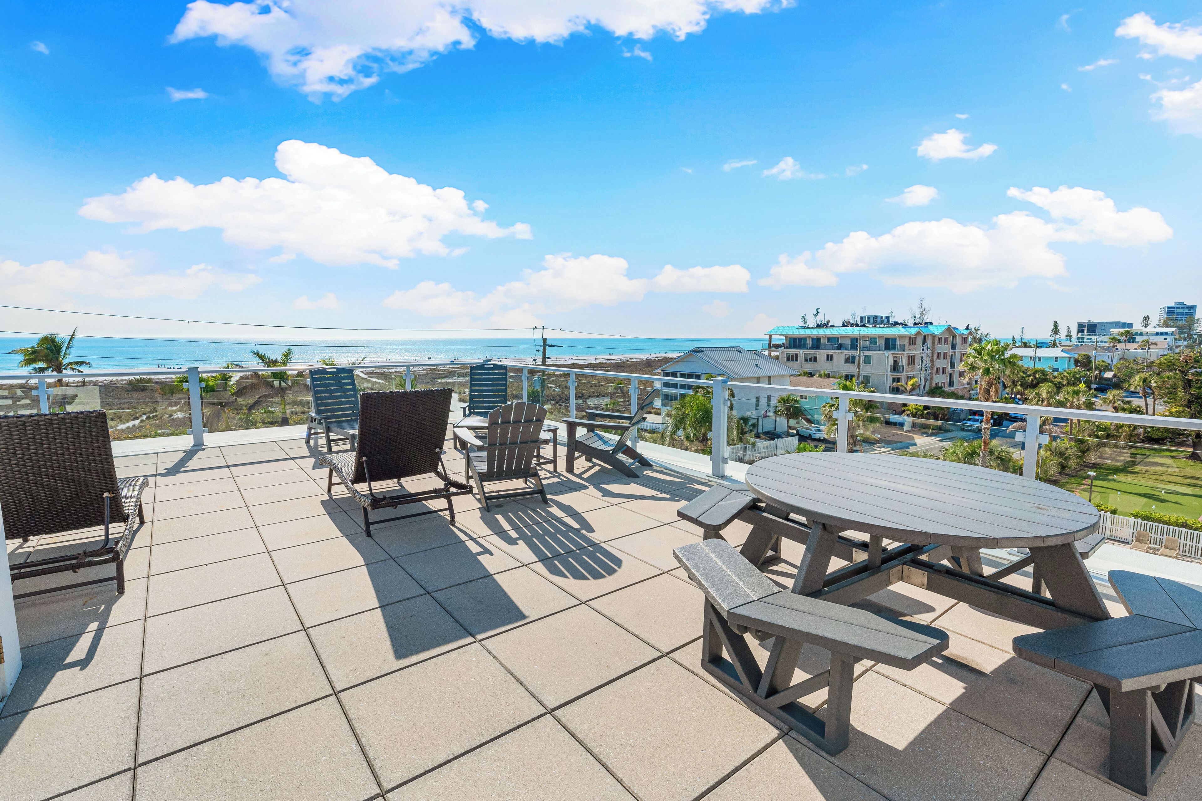 A patio with outdoor seating, a view of the ocean, and a building in the background.