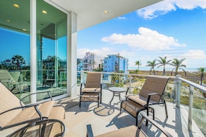 Un balcón con puertas de cristal, mobiliario exterior y vistas a la playa y edificios.