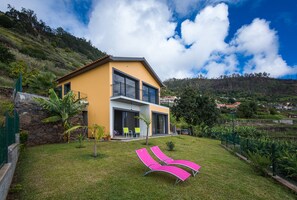 A two-story house with a balcony, surrounded by a well-maintained lawn and tropical plants.
