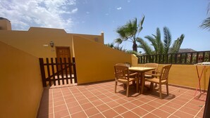 Un patio con suelo de baldosas, una mesa y sillas de madera, y una reja.