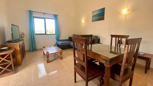 Una sala de estar con una mesa de comedor, sillas, un sofá, un televisor y una ventana con cortinas.