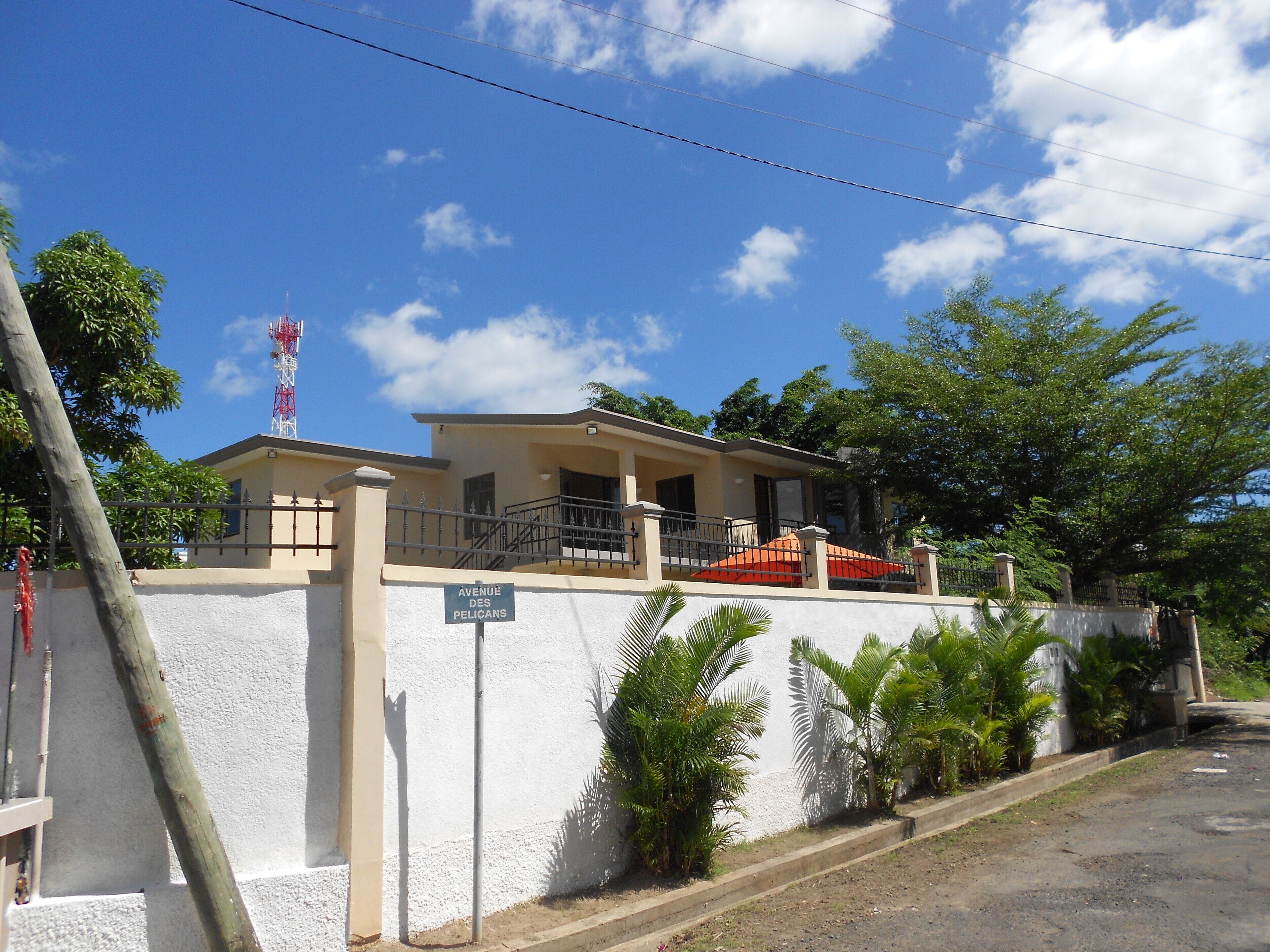 A two-story building with a balcony, a sign reading "Avenue des Pelicans," and a red car parked in front.