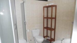 Ein Badezimmer mit Dusche, zwei Toiletten und einem Holzregal.