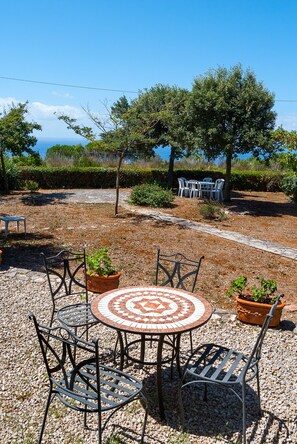 Eine Terrasse mit rundem Tisch und Stühlen, umgeben von Kübelpflanzen und Blick auf das Meer.