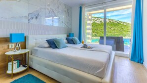 Un dormitorio moderno con una cama grande, una mesita de noche y vistas a un paisaje verde a través de un ventanal amplio.