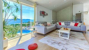 Una sala de estar moderna con un amplio ventanal que ofrece una vista panorámica, un sofá modular gris, una mesa de centro blanca y una alfombra estampada.