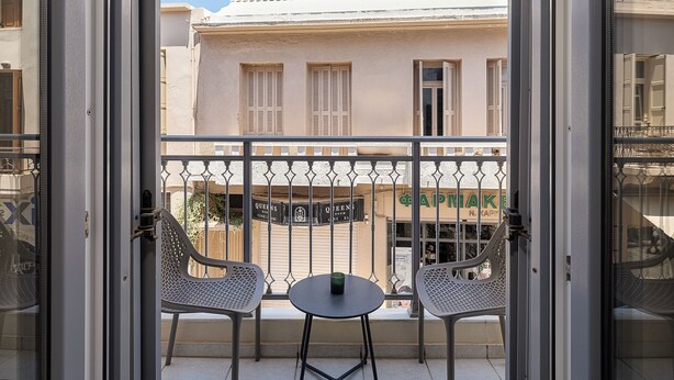 A balcony with two chairs and a small table, overlooking a building with a sign reading "CAPMAKE".