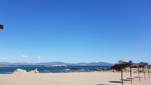 A beach with clear skies, a rocky shoreline, and thatched umbrellas.