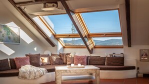 A cozy living room with a sloped ceiling, a large window offering a view of the outdoors, a sofa with cushions, and a coffee table. - Fantastic apartment in Goslar am Harz (Goslar-Jerstedt)