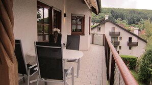 A balcony with a table and chairs, overlooking a residential area with houses and greenery. - Modern spacious apartment in a quiet south-facing slope. (Kandern)