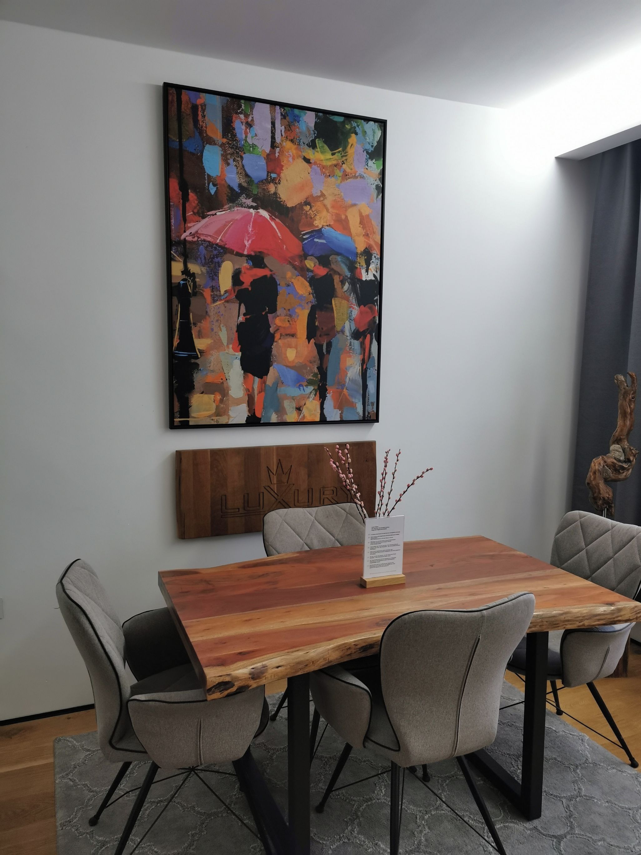 A conference room with a wooden table, grey upholstered chairs, and a colorful abstract painting on the wall.