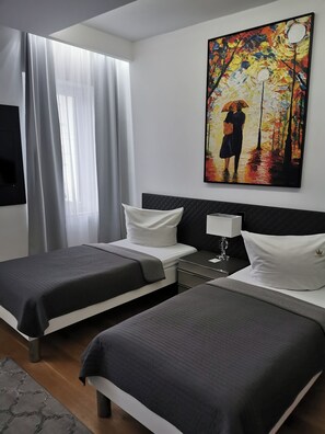 A hotel room with two beds, a painting on the wall, a desk with a lamp, and a TV mounted on the wall. - Comfortable Apartments Studio 2 (Leipzig)
