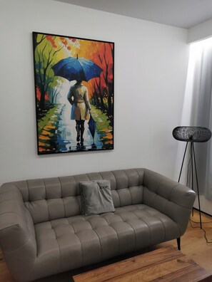 Una sala de estar moderna con un sofá gris, un cuadro de una mujer con un paraguas y una lámpara de pie.