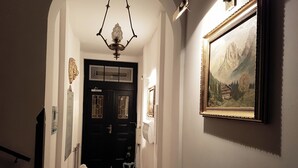Un couloir avec une porte noire, une moquette rouge, un lustre et un tableau encadré accroché au mur.