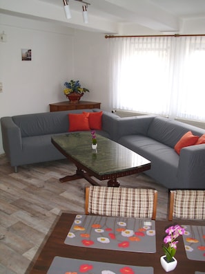 Una sala de estar con un sofá gris, una mesa de centro de madera y una mesita blanca con un mantel decorado con flores.