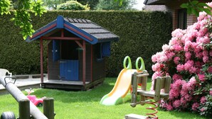 Un área infantil con un tobogán, una casita de madera y columpios.