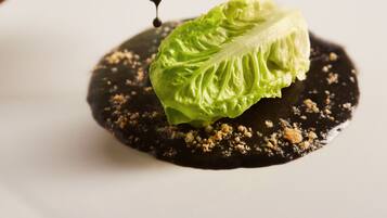 A dish with a green leafy vegetable on a dark sauce with crumbled topping.