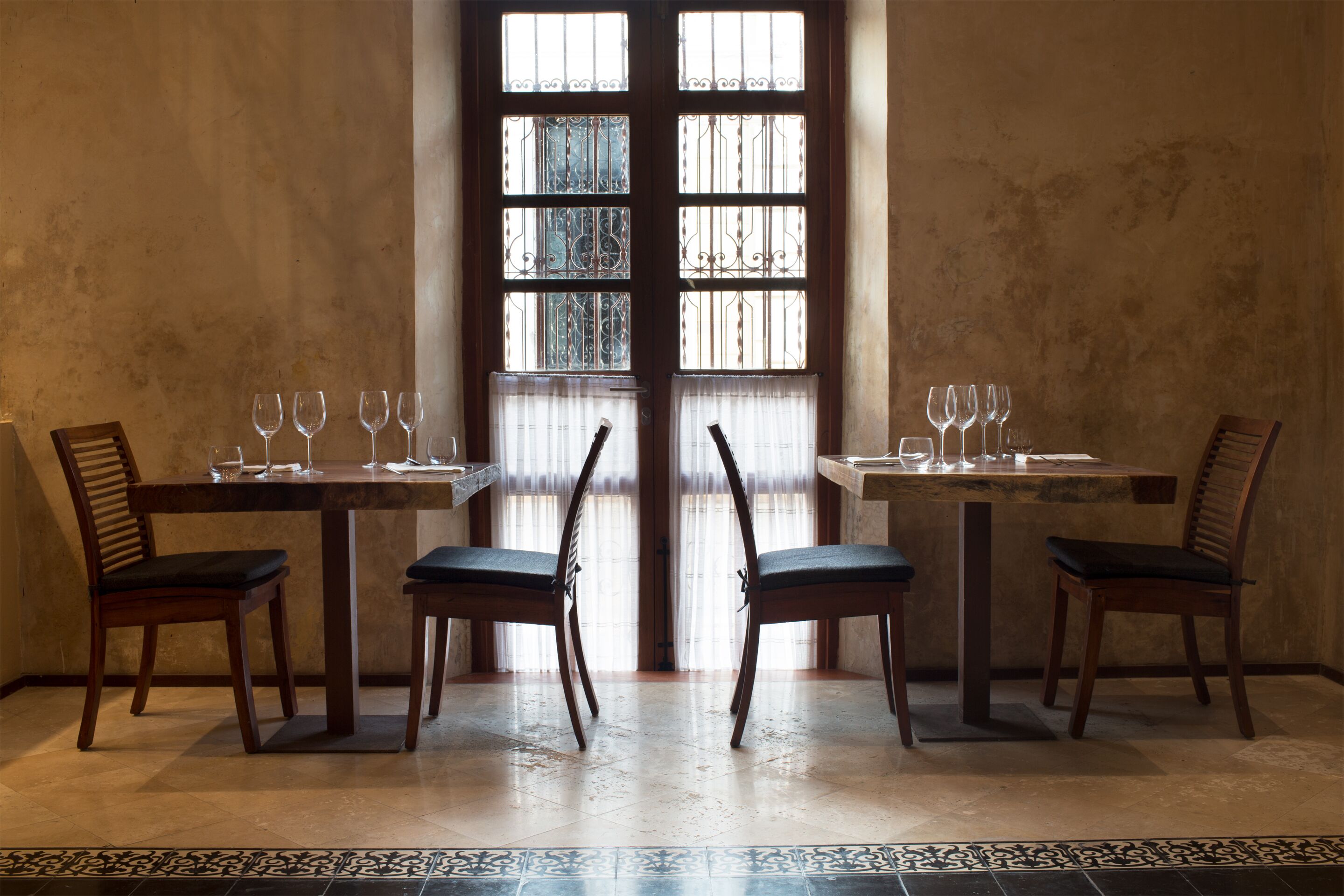 A dining area with two tables, each with four chairs, and a large window with bars.