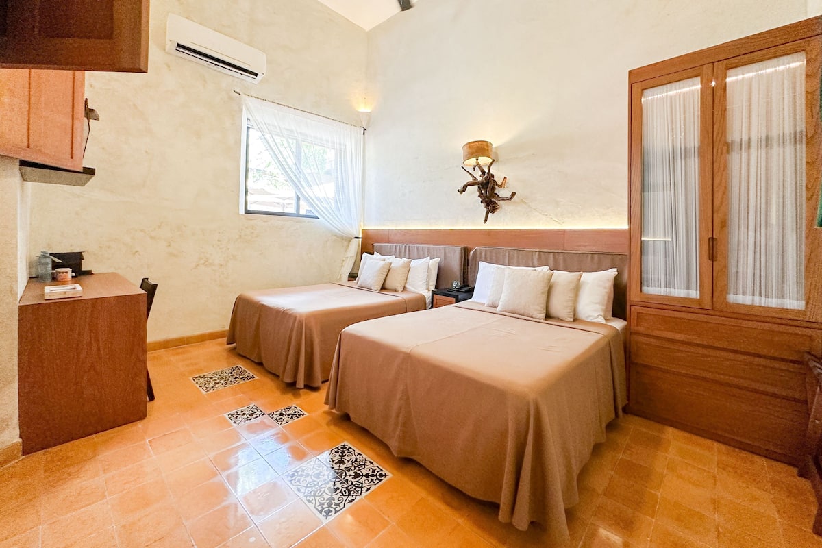 A hotel room with two beds, a desk, an air conditioning unit, a window with curtains, a ceiling fan, and a cabinet.