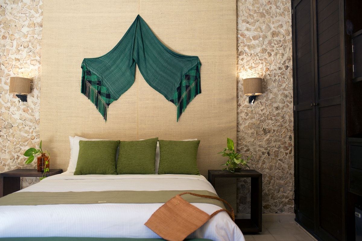 A neatly made bed with green pillows, a decorative green fabric hanging above, and two bedside lamps.
