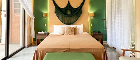 A hotel room with a large bed, a bench, a green wall, and a window with curtains.