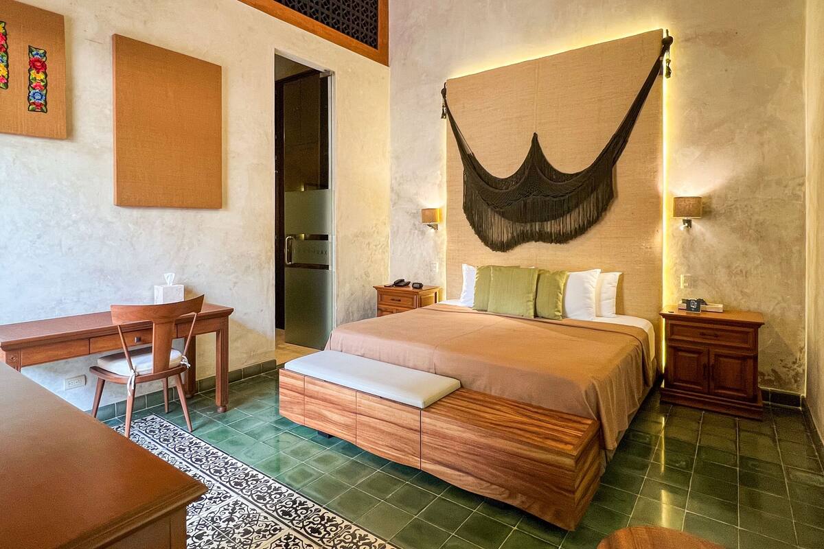 A hotel room with a bed, bedside tables, a desk, a chair, and a large woven hanging chair.