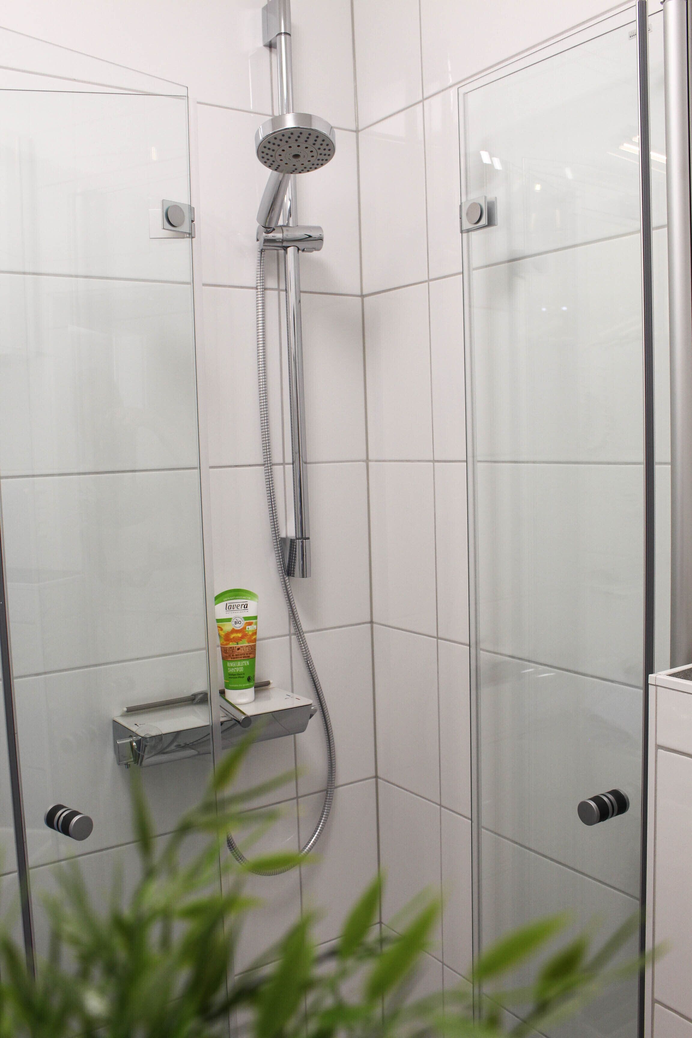 Een moderne douche met een handdouche, een glazen douchecabine en een zeepdispenser aan de muur.