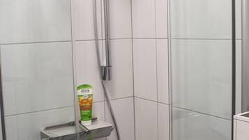 Een moderne douche met een handdouche, een glazen douchecabine en een zeepdispenser aan de muur.