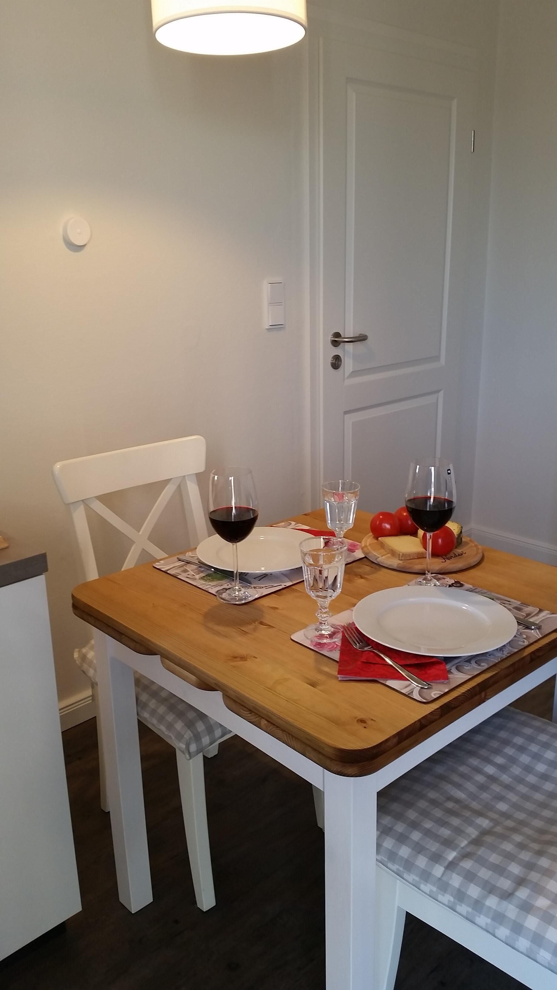 Een eettafel gedekt met borden, glazen en bestek, een stoel en een deur op de achtergrond.