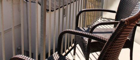 A balcony with wicker furniture and a view of a green landscape.