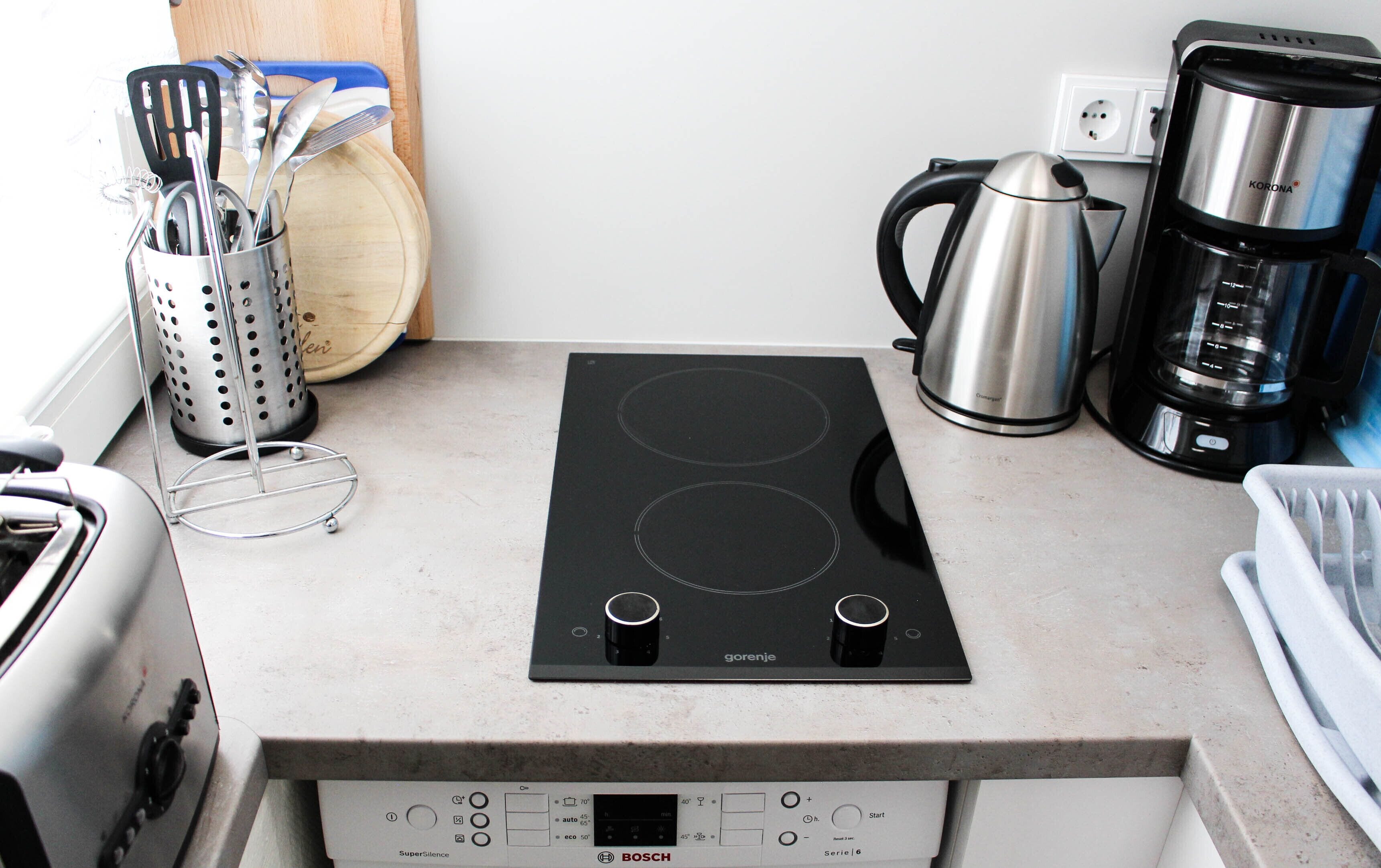 A kitchen with a black induction cooktop, a stainless steel kettle, a coffee maker, and a utensil holder.
