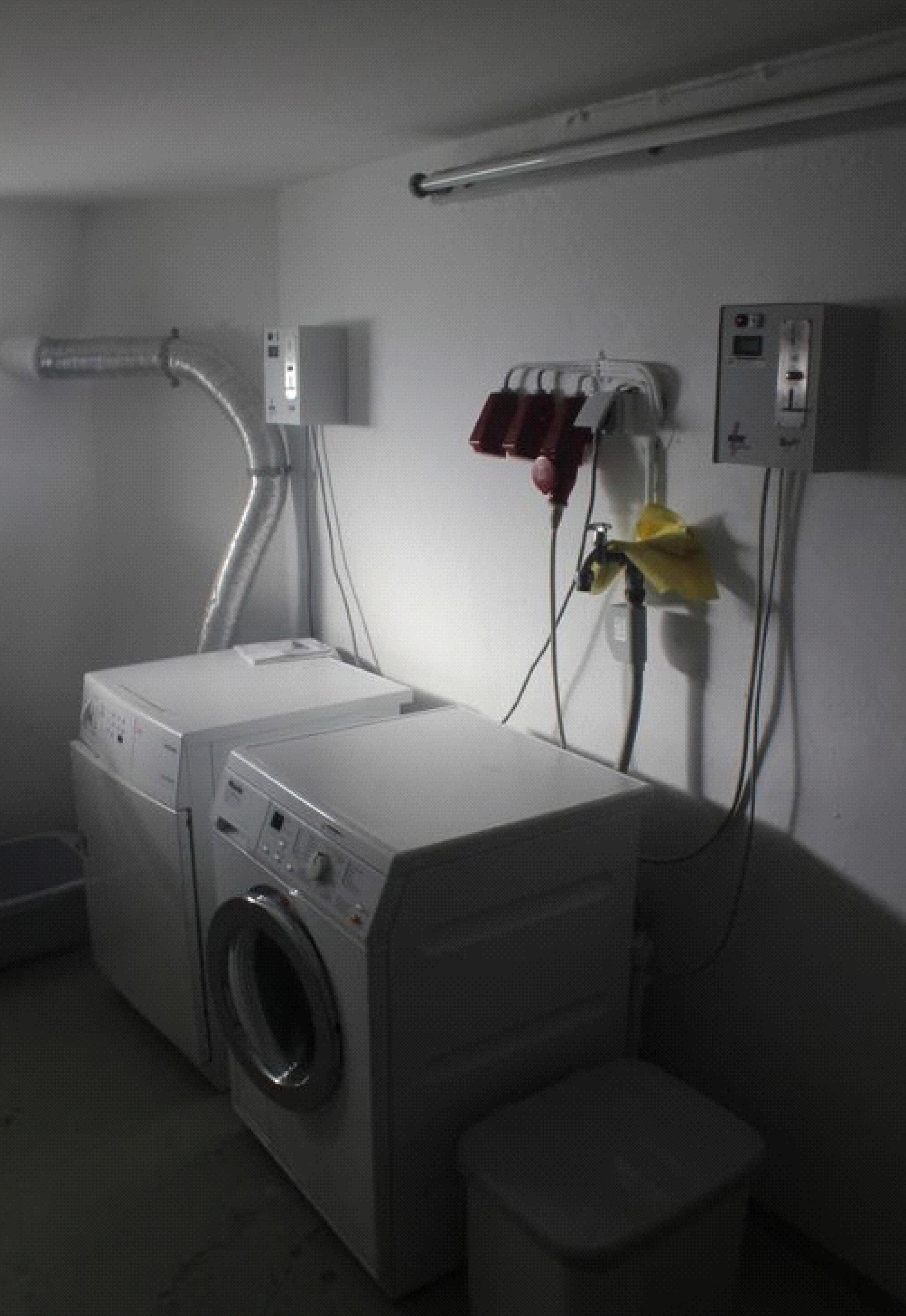 A laundry room with a front-loading washing machine, a dryer, and a utility wall with electrical outlets and a vent.