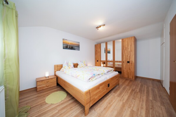 A bedroom with a wooden bed, a nightstand, a mirror, and a green curtain.