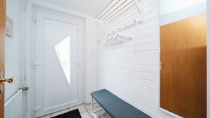 A room with a white door, a bench, a drying rack, and a wooden door.