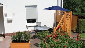 A patio with a table and chairs, a wooden fence, and potted plants.