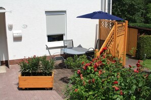 A patio with a table and chairs, a wooden fence, and potted plants.